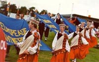 Trachtenpaare aus den Baltischen Staaten tragen Fahnen mit den früheren Europeade-Städten